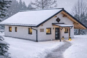 A snow-covered building with a sloped roof, a front porch, and multiple windows. - Holiday home ViaNova (Mauth)
