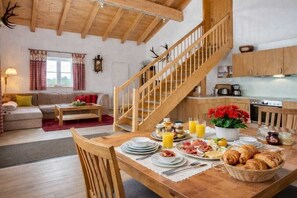 A cozy living room with a wooden staircase, a dining area with breakfast, and a kitchen with wooden cabinets. - Holiday home ViaNova (Mauth)