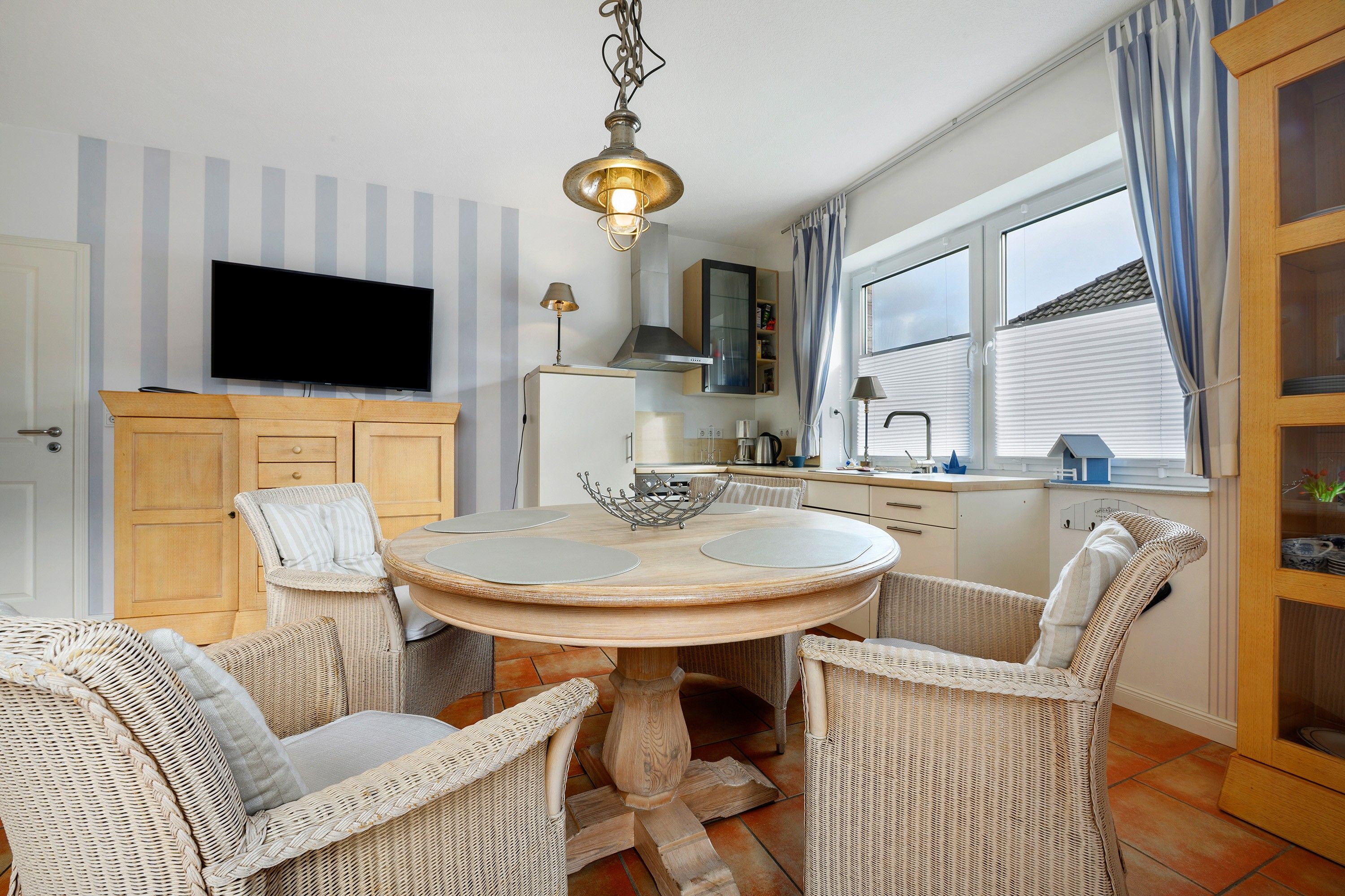 A dining area with wicker chairs, a round table, and a television mounted on the wall.
