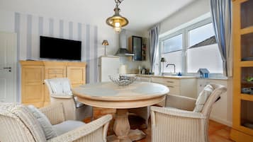 A dining area with wicker chairs, a round table, and a television mounted on the wall.