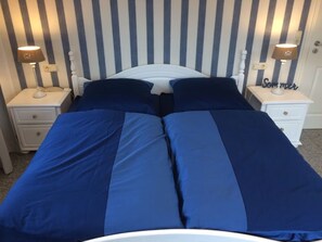 Ein Doppelbett mit blauer Bettwäsche, zwei Nachttische mit Lampen und eine gestreifte Wand.
