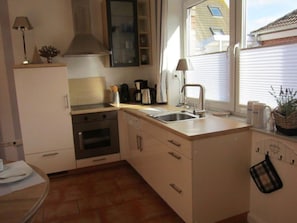 Eine kleine Küche mit Herd, Backofen, Spüle und einem Fenster für natürliches Licht.