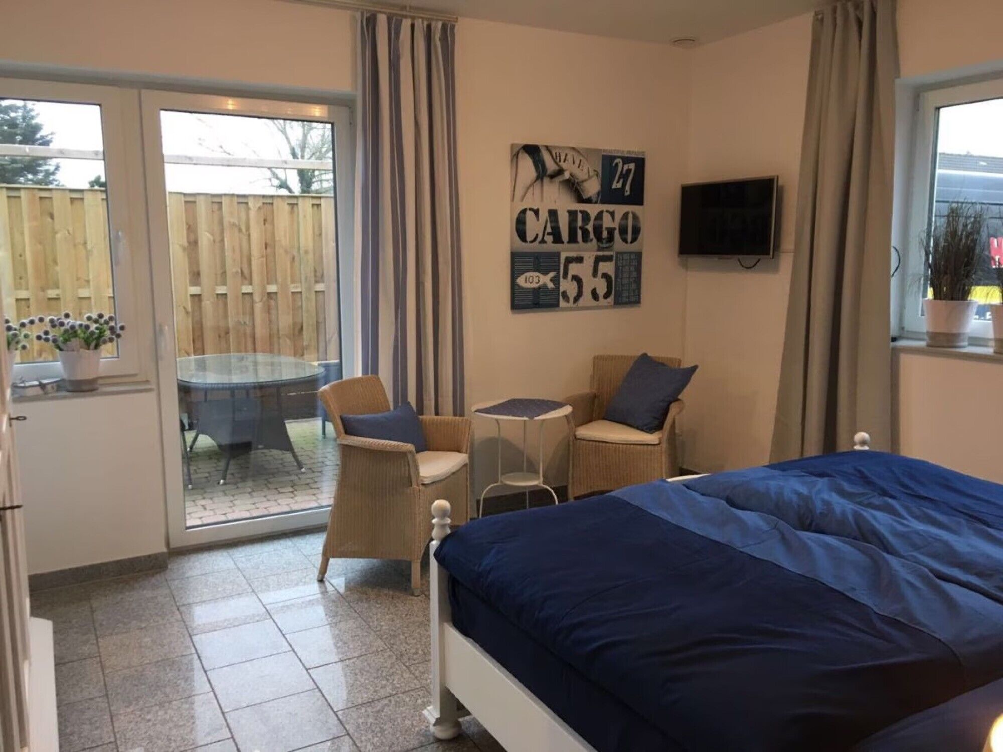 Ein Schlafzimmer mit einem Bett, einem kleinen Tisch, zwei Stühlen, einem Fernseher und einer Glastür zu einer Terrasse.