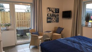 A bedroom with a bed, a small table, two chairs, a television, and a sliding glass door leading to a patio. - Apartment 'Anna Sandbank' with Private Terrace, Private Garden and Wi-Fi (Krummhörn)