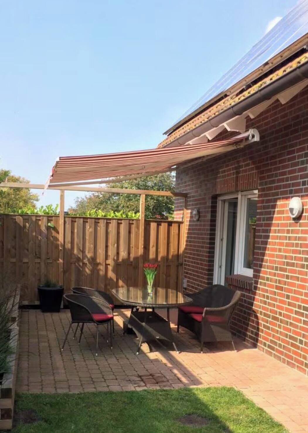 Eine Terrasse mit einem Glastisch und Stühlen, einem Holzzaun und einem Backsteinhaus.