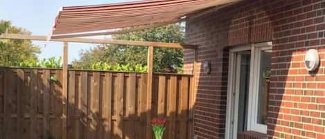Eine Terrasse mit einem Glastisch und Stühlen, einem Holzzaun und einem Backsteinhaus.