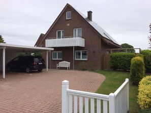 Ein zweistöckiges Haus mit überdachter Auffahrt, weißem Zaun und einem gepflegten Garten.