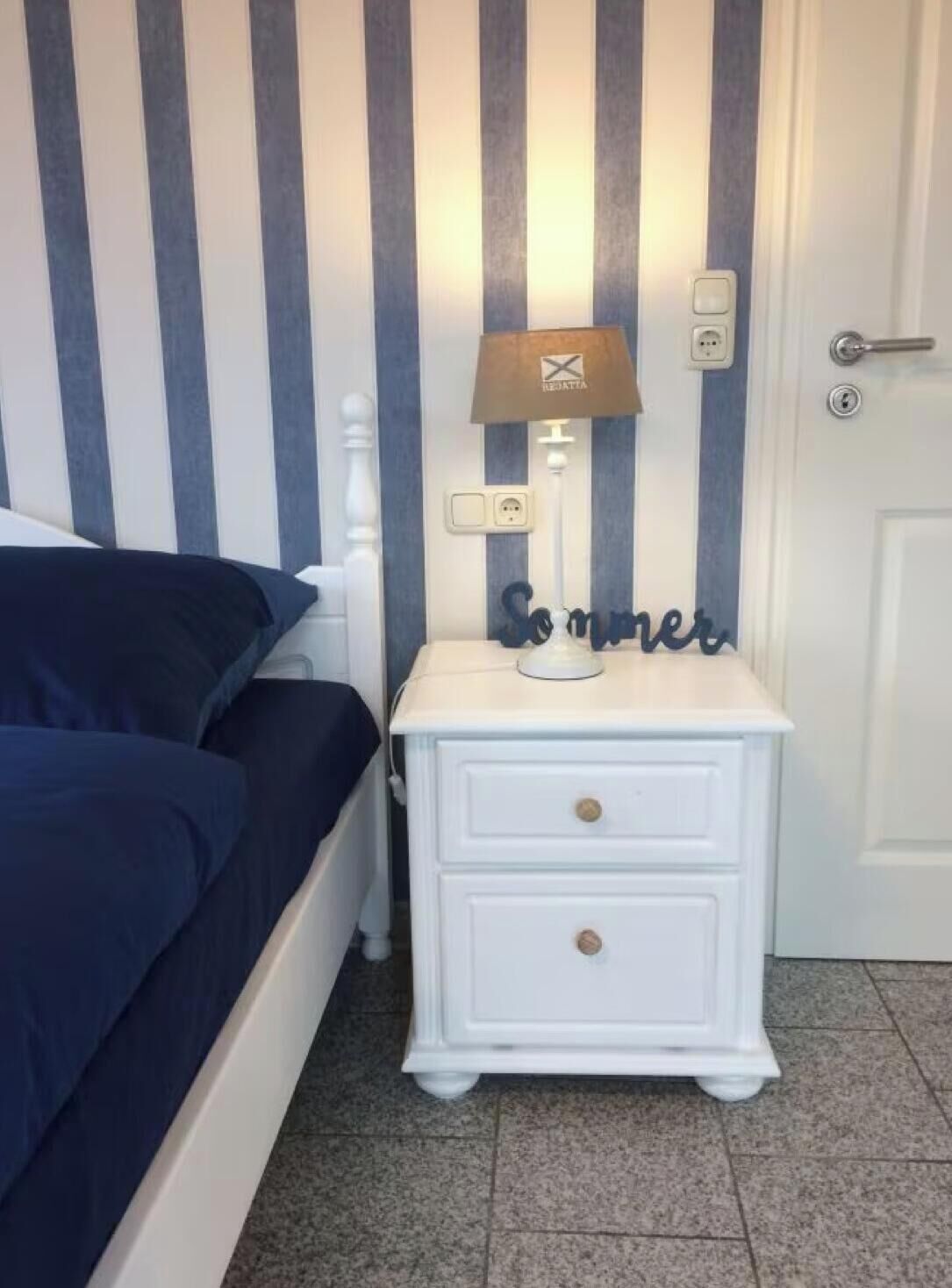 Une chambre à coucher avec un lit, une table de chevet avec une lampe et un mur à rayures verticales.
