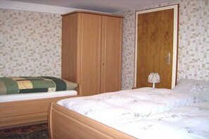 Een slaapkamer met een eenpersoonsbed, een houten garderobe en een deur met een handgreep.