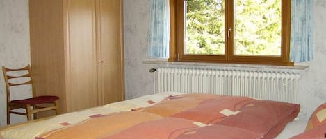 Un dormitorio con cama, armario, silla y ventana con vistas a árboles.