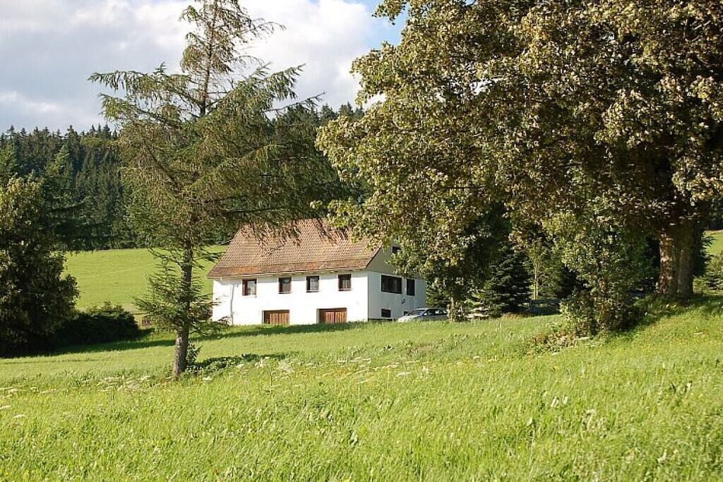 Un bâtiment blanc avec un toit rouge, entouré d’herbe verte et d’arbres.