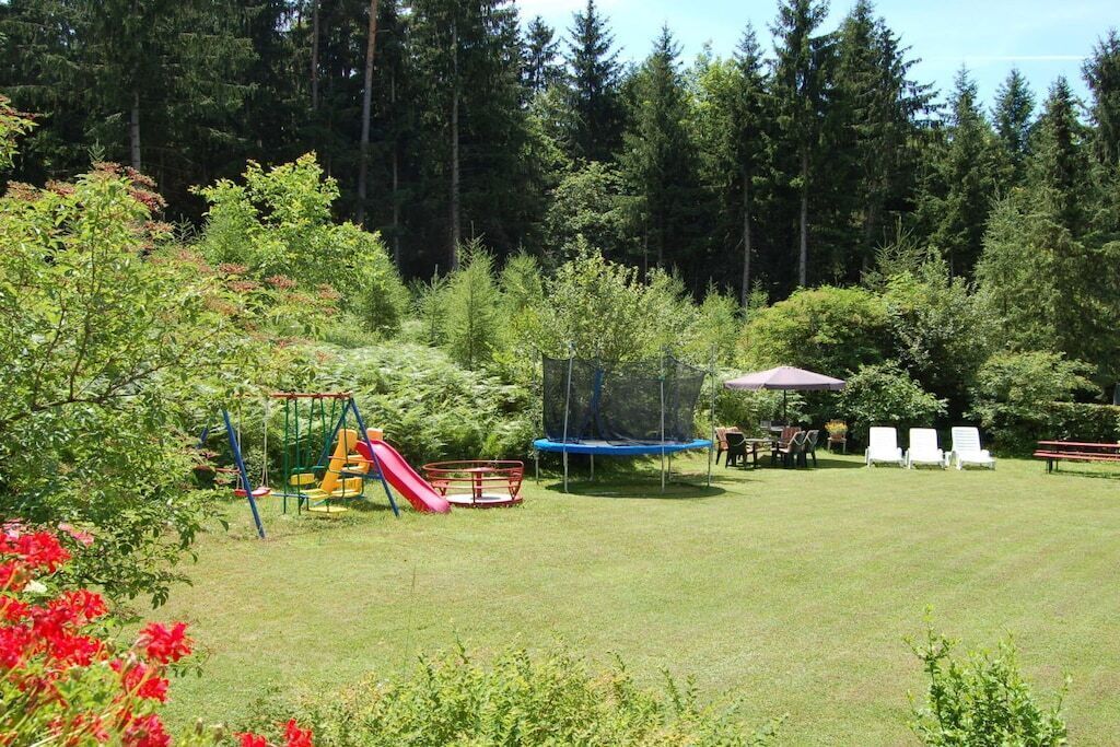 A grassy outdoor area with a playground including a slide and swings, surrounded by trees.