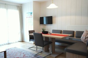 Uma sala de estar moderna com mesa de jantar, sofá e televisão.