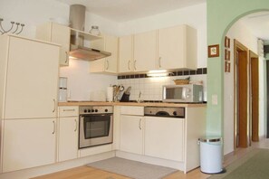Uma cozinha compacta com armários brancos, fogão, forno, micro-ondas e lixeira.