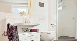 A bathroom with a white sink, a mirror, a toilet, and a shower area. - Wattkieker de Ool in the Vitamar holiday park (Wurster Nordseeküste)