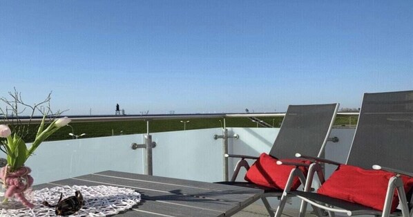A balcony with a table, two chairs with red cushions, and a view of the horizon. - Wattkieker de Ool in the Vitamar holiday park (Wurster Nordseeküste)