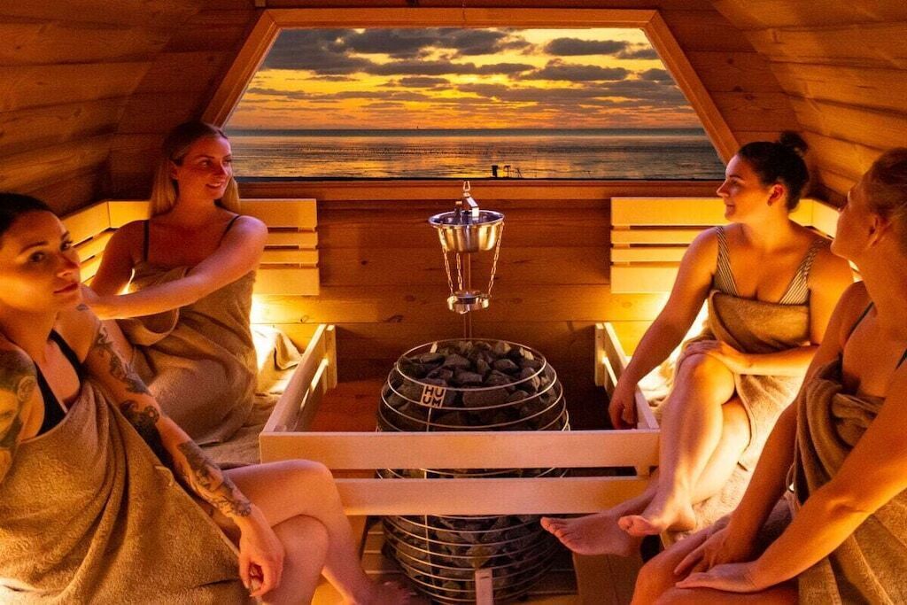 A group of people sitting in a wooden cabin with a view of the sunset through a window.