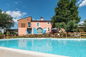 Ein Schwimmbecken mit Holzzaun, ein Gebäude mit blauen Türen und ein klarer, blauer Himmel.