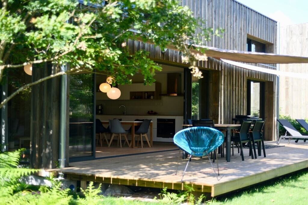 Un espace de restauration extérieur moderne, doté d’une terrasse en bois, de chaises à structure métallique et d’une véranda en verre.