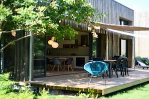 A modern outdoor dining area with a wooden deck, metal-framed chairs, and a glass enclosure. - Bioclimat wooden house in the countryside (Messanges)