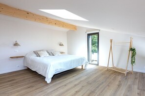 A bedroom with a bed, wooden beams, a window, and a plant stand. - Bioclimat wooden house in the countryside (Messanges)
