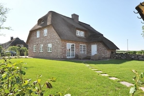 Une maison à deux étages, avec une façade en briques, un toit de chaume et une pelouse bien entretenue.