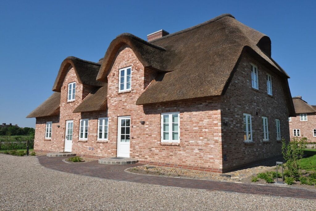 Ein Backsteinhaus mit Strohdach und Kiesauffahrt.