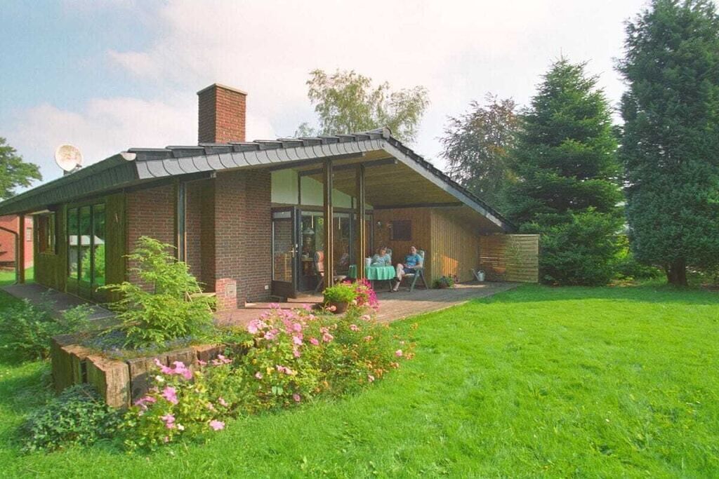Ein eingeschossiges Backsteingebäude mit überdachter Terrasse, umgeben von einem gepflegten Rasen und Garten.