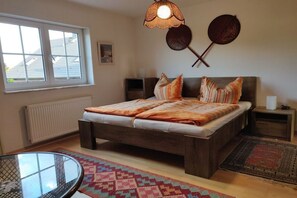 Een slaapkamer met een houten bed, een rond glazen tafeltje, een raam en een radiator.