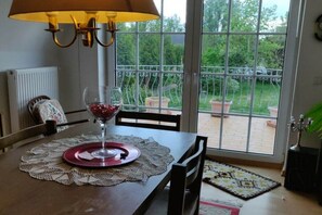 Een eettafel met een glas rode wijn, een kant kleed en uitzicht op een tuin door een glazen deur.