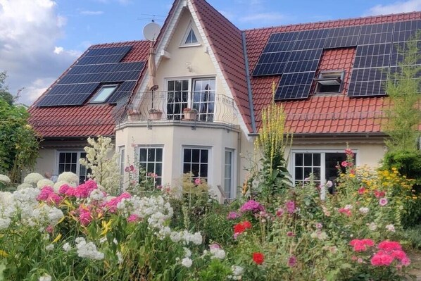 Een huis met een rode pannendak, zonnepanelen en een tuin met verschillende bloemen.