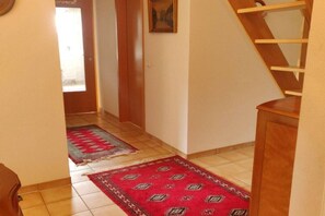 A hallway with a wooden staircase, a red patterned rug, and a painting on the wall. - Holiday apartment with 2 bedrooms (Oberkrämer)