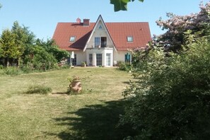 Een huis met een rood pannendak, een veranda en een verzorgd gazon.