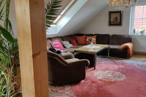 Een knus loft-stijl woongedeelte met een schuin dak, een bruine zithoek, een salontafel en een groot raam met uitzicht.