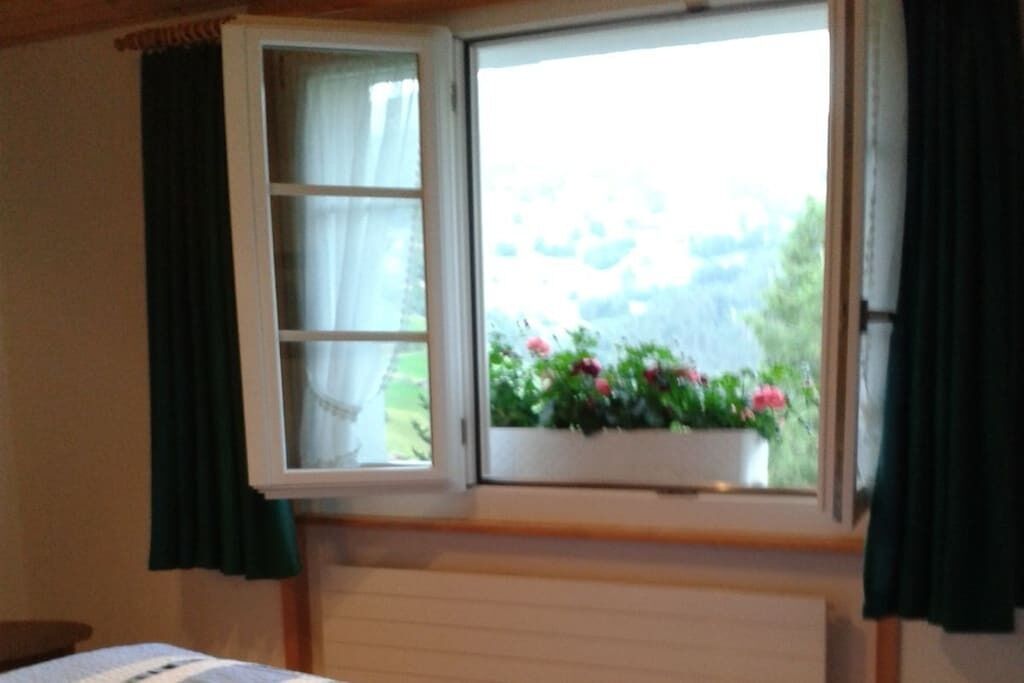 Ein Zimmer mit einem Bett, einem Vorhangfenster und Blick auf Grünfläche.