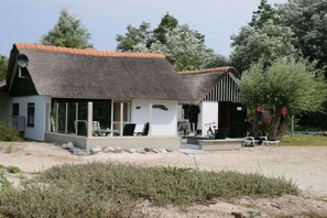 A house with a thatched roof, a covered porch, and a small garden area. - Cabin in Makkum with swimming pool (Makkum)