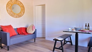 A room with a grey sofa, a round mirror, a dining table with chairs, and a bench. - Holiday home apartment with 2 bedrooms on the beach (Piana)