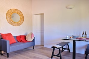 Una habitación con un sofá gris, un espejo redondo, una mesa de comedor con sillas y un banco.