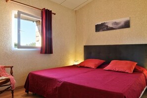 Ein Schlafzimmer mit einem Bett, einem Fenster mit Vorhängen, einem Sessel und einem an der Wand hängenden Bild.