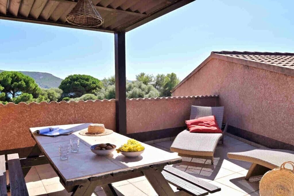 An outdoor patio with a table set for two, a cushioned seating area, and a view of the surrounding landscape.