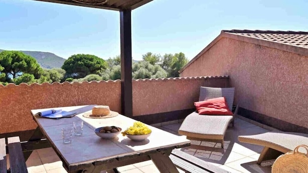 An outdoor patio with a table set for two, a cushioned seating area, and a view of the surrounding landscape. - Holiday home apartment with 2 bedrooms on the beach (Piana)