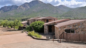 A building with a stone facade, a patio area, and a view of mountains in the background. - Holiday home apartment with 2 bedrooms on the beach (Piana)