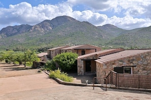 Un edificio con fachada de piedra, un patio y vistas a montañas al fondo.