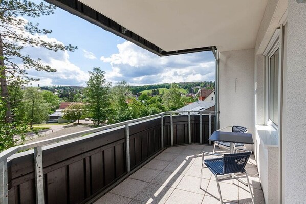 Un balcon avec une table et des chaises, une vue sur un paysage verdoyant et un ciel dégagé.