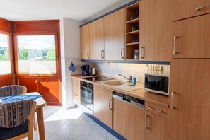 Une cuisine avec des meubles en bois, un lave-vaisselle, un four à micro-ondes et une fenêtre donnant sur un espace verdoyant.