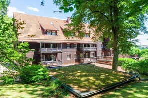 A multi-story building with a sloped roof, balconies, and a courtyard with a grassy area. - Holiday apartment with 3 bedrooms (Braunlage)