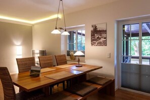 A dining area with a wooden table, woven chairs, and a bench. There is a lamp on the table, and a window with blinds to the right. - Holiday apartment with 3 bedrooms (Braunlage)