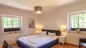 Quarto com cama, mesas de cabeceira, uma cadeira e janelas.