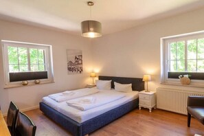 A bedroom with a bed, bedside tables, a chair, and windows. - Holiday apartment with 3 bedrooms (Braunlage)
