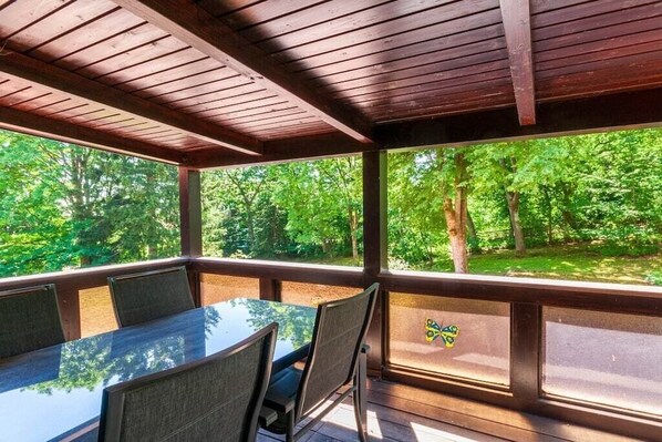 A covered outdoor dining area with a table and chairs, large windows, and a view of a wooded area. - Holiday apartment with 3 bedrooms (Braunlage)